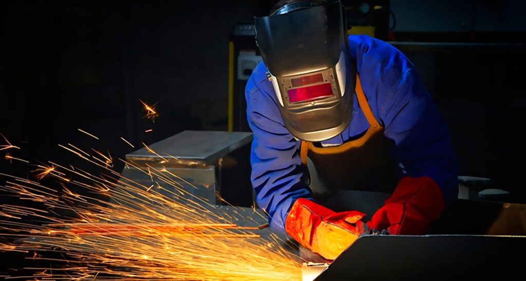 man in helmet, jacket, and gloves welding